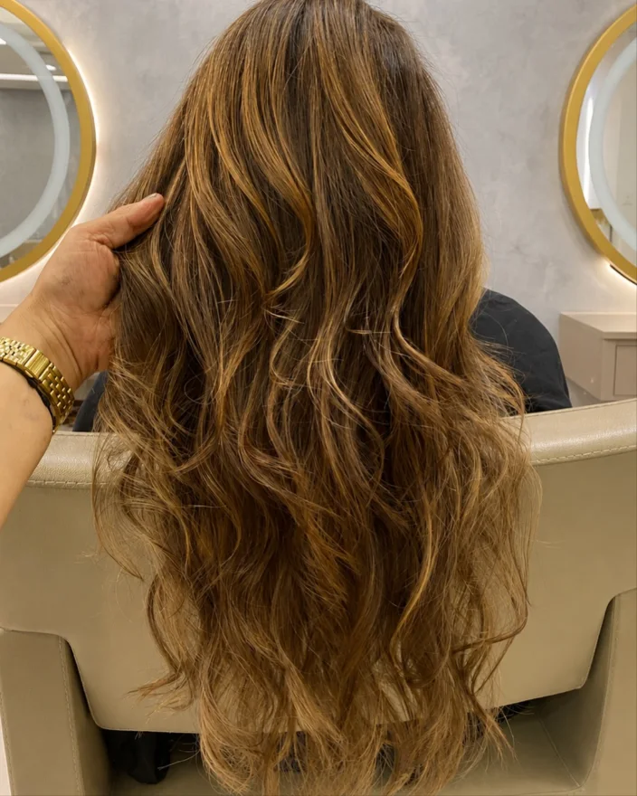 Cabelo iluminado com ondas, visto de costas na cadeira do salão